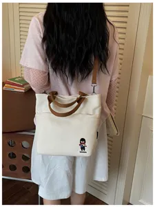 Détail du sac bandoulière en toile avec motif brodé et lanières marron résistantes.