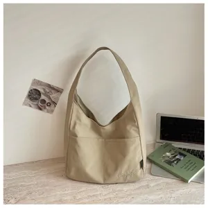 Detailaufnahme der beigen Canvas-Schultertasche mit Vordertasche und feiner Stickerei.