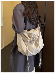 Vue détaillée d'un sac bandoulière minimaliste beige à cordon de serrage porté sur l'épaule.
