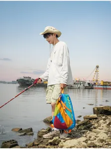 Outdoor lifestyle detail view showing the colorful folding backpack worn by the riverbank.