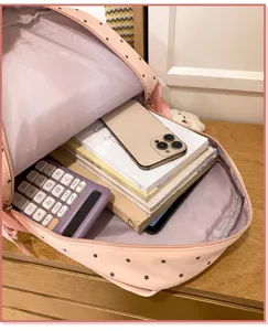 Gedetailleerd overzicht van het ruime interieur van een schattige roze rugzak met stippen en boeken.