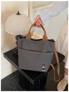 Vue détaillée du sac cabas en toile grise avec anses marron et une poche zippée avant.