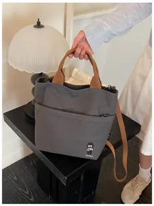 Détail de la pochette fourre-tout en toile grise épaisse avec anses marron et jolie broderie.