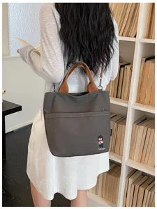 Vue détaillée du sac cabas en toile grise avec anses marron et petit patch décoratif.