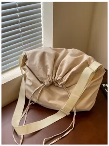 Sac bandoulière beige à cordon de serrage, tissu souple, large sangle et grande capacité de rangement.