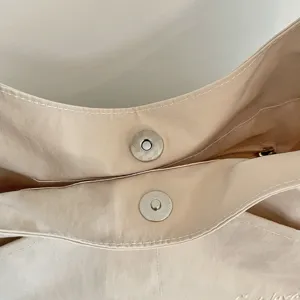 Minimalistische beige Segeltuch Schultertasche mit magnetischem Druckknopf und feiner Textur.