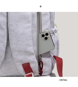 Grey canvas backpack detail showing zipper side pocket and durable red strap for daily use.