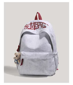 Grey canvas backpack detail featuring red embroidered letters and a cute plush bear pendant.