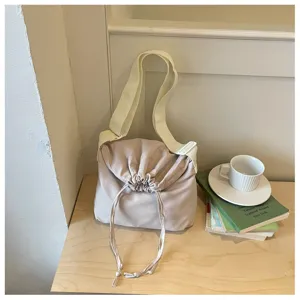Vue détaillée du sac bandoulière beige à cordon dans scène lifestyle avec livres et tasse.