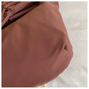Gros plan du détail du sac bandoulière marron avec texture de tissu douce et plis élégants.