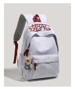 Detail view of grey student backpack featuring red embroidered letters and a cute bear pendant.