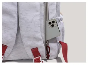 Close-up detail of grey canvas backpack with red straps and side zipper pocket holding phone.