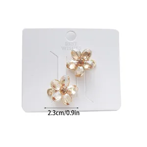 Detailed closeup of sparkly crystal flower hair clip with golden setting on white display card.