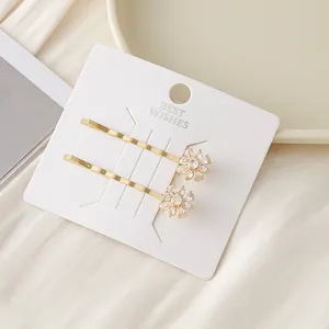 Pinces à cheveux dorées ornées de fleurs en zircone éclatantes sur carte blanche.