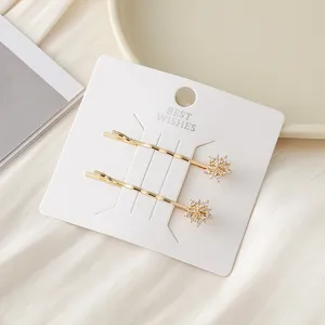Vue détaillée de pinces à cheveux dorées avec zircons flocon de neige sur carte de présentation.
