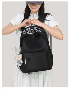 Detail shot of black canvas backpack with embroidery letters and cute bear pendant for daily use.