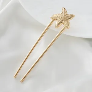 Gold starfish hair pin detail, elegant metal U-shaped hair fork closeup view on white cloth.