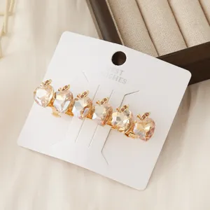 Close-up detail of luxury crystal apple hair clip with gold metal finish on white card.