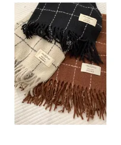 Detailed shot showing the soft texture, fringe design and brand label of the plaid winter scarf.