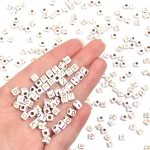 Close-up detail of white square acrylic letter beads with gold text for DIY jewelry making.