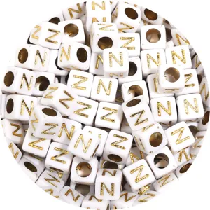 Close-up detail of white square acrylic beads with gold letters for DIY jewelry making.