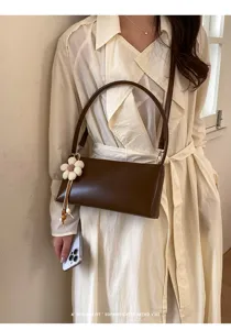 Detailed shot of retro PU leather shoulder bag with chic flower charm and sleek strap.