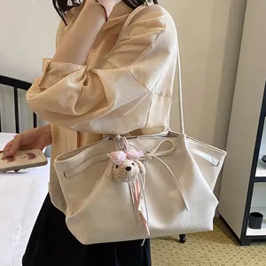 Detail view of the elegant beige tote bag with cute puppy plush pendant and chic bow.