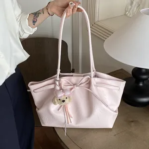 Pink PU leather tote bag detail with cute bow tie and plush bear charm on wooden table.