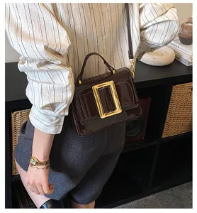 Detail shot of the vintage patent leather handbag featuring a striking gold rectangular buckle.