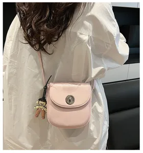 Close-up of pink leather crossbody phone bag with metal twist lock and cute doll pendant.