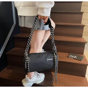 Black cylindrical shoulder bag with chunky braided straps in a stylish stair setting.