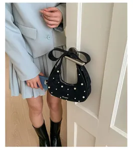 Detailed view of trendy black quilted shoulder bag with pearl decor and bow design.