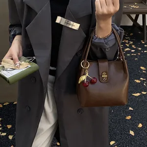 Detail view of stylish retro women's bucket bag in dark brown PU leather with cherry charm.