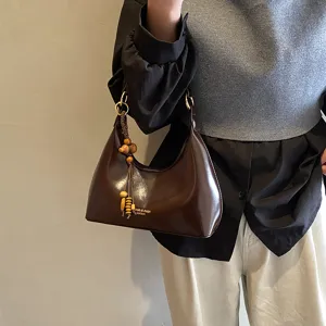 Detailed view of brown leather underarm bag with wooden bead tassel charm and smooth finish.