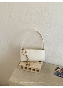 Minimalist retro white shoulder bag detail shot featuring a chic floral charm on textured stone.