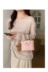 Detailed view of pink top-handle lock box bag featuring cute fluffy charm and cozy knit apparel.
