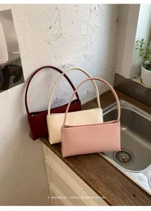 Detailed view of minimalist retro PU shoulder bags in three chic colors on a wooden surface.