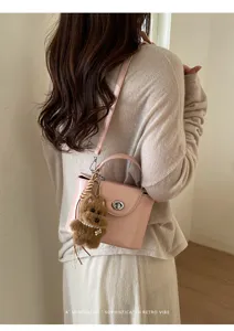 Stylish pink crossbody bag with lock closure and cute plush bear charm for daily commute.