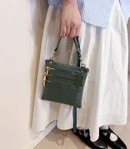 Detailed view of the dark green leather multi-pocket cross-body bag showing metal zippers.