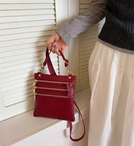 Red leather crossbody bag detail, multi zipper compartments, elegant fashion accessory.