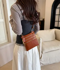 Detailed view of women brown leather crossbody bag showcasing multiple front zipper pockets.