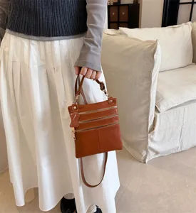 Detail view of the brown leather crossbody bag featuring multiple secure zipper pockets for daily use.