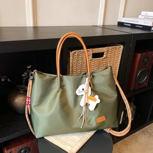 Vue détaillée du sac cabas en nylon vert avec poignées marron, charm et sangle robuste.