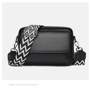 Elegante bolso bandolera de cuero negro para mujer con correa ancha estampada.
