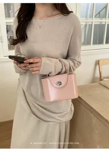 Detailed close-up of pink structured box handbag with metallic turn-lock in indoor setting.