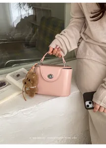 Detailed view of the pink structured top-handle box bag with elegant turn-lock and cute bear charm.