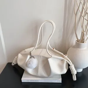 Close up detail of white soft leather cloud shoulder bag with dual handles and fluffy pompom charm.