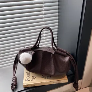 Brown soft leather shoulder bag with pleated design and plush ball pendant for women.