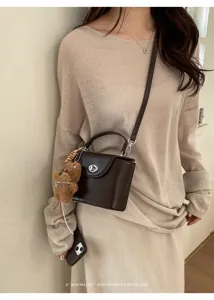Dark brown structured box crossbody bag with lock closure and cute bear charm pendant detail.