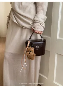 Stylish brown turn-lock handbag with cute plush bear charm for women daily commuting chic.